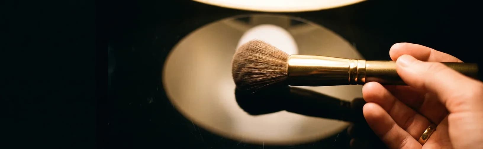 A single makeup brush laid flat on glossy black glass, lit from above